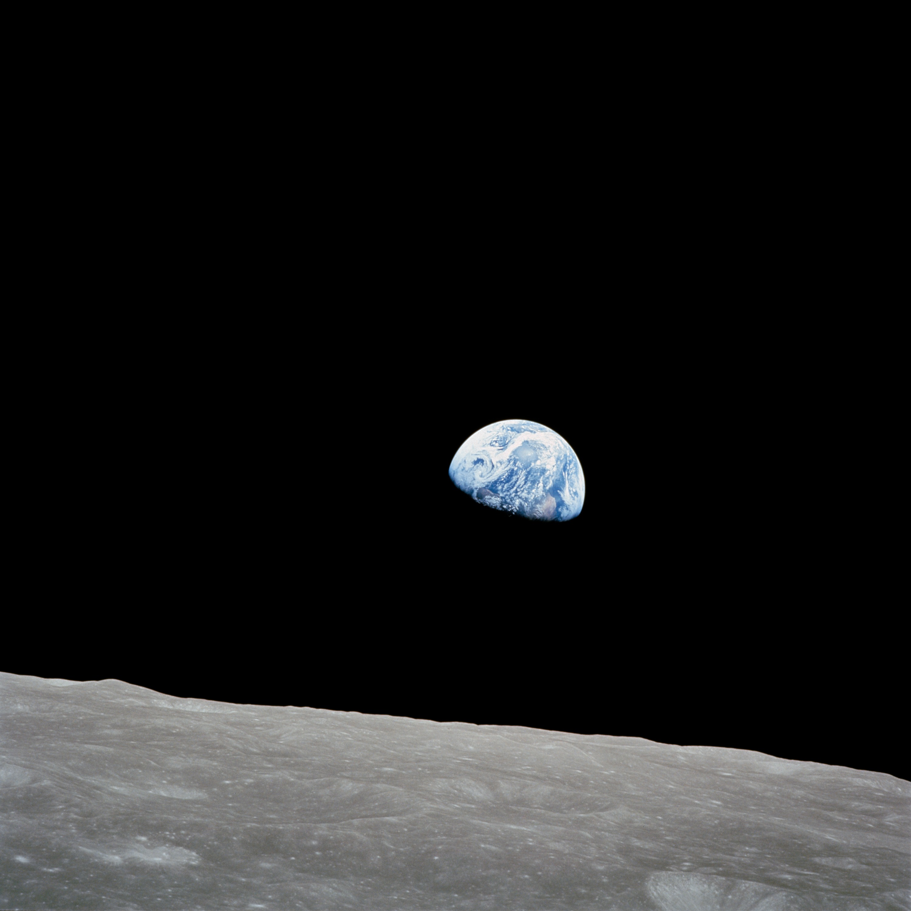 Earthrise: the blue and white earth rising above the gray cratered horizon of the moon, photographed from lunar orbit